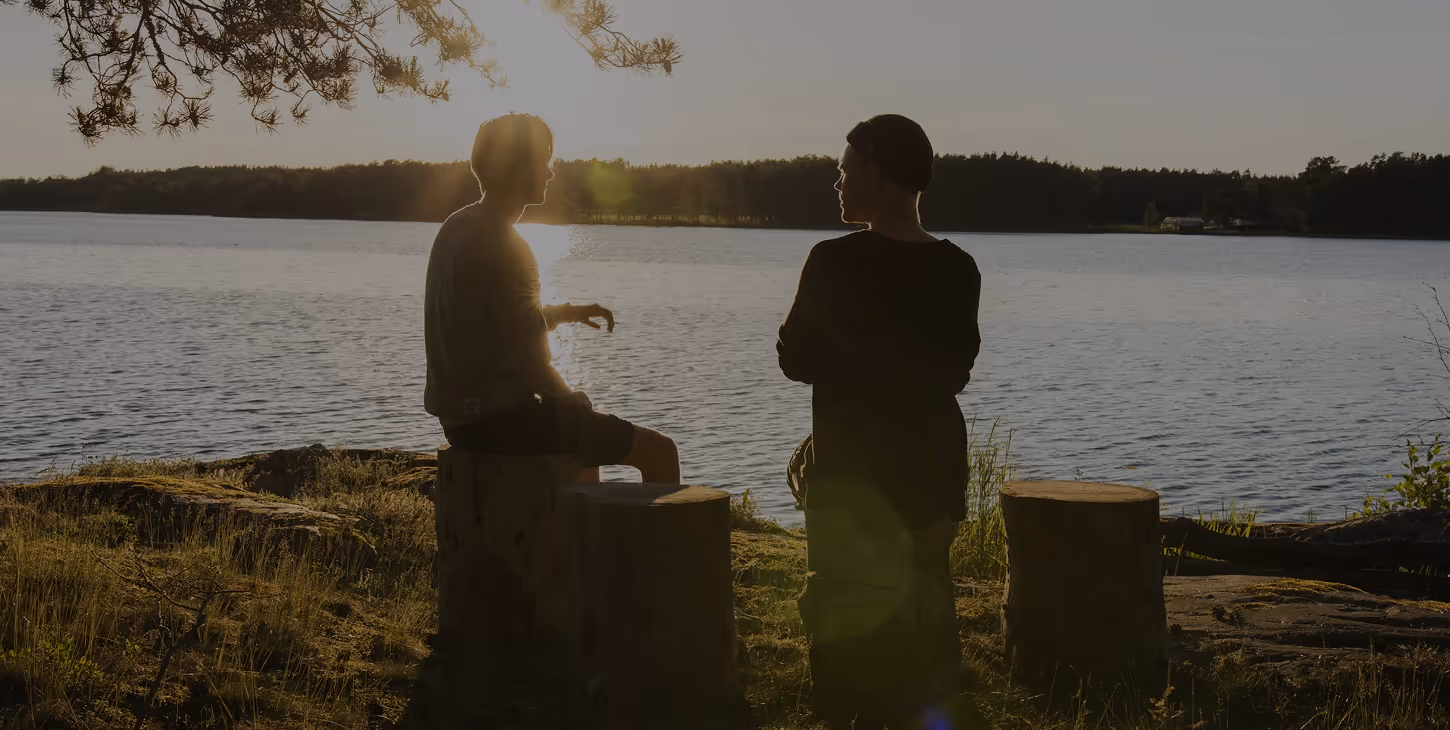Two people talk beside a lake at sunset